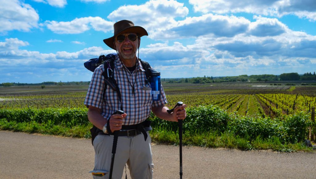 Randonneur souriant à la caméra. Derrière lui, des vignes à perte de vue.